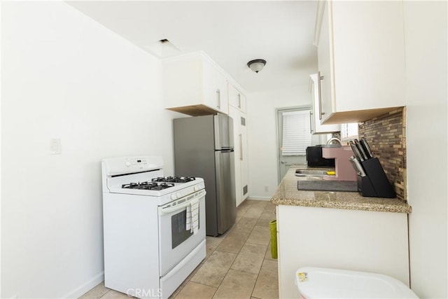 kitchen with sink, gas range gas stove, white cabinetry, stainless steel refrigerator, and backsplash