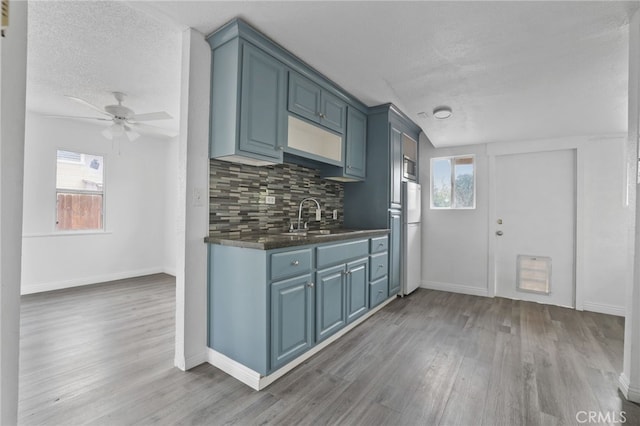 kitchen featuring sink, blue cabinetry, hardwood / wood-style floors, white refrigerator, and decorative backsplash