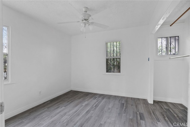 empty room featuring ceiling fan, wood-type flooring, a textured ceiling, and a wealth of natural light