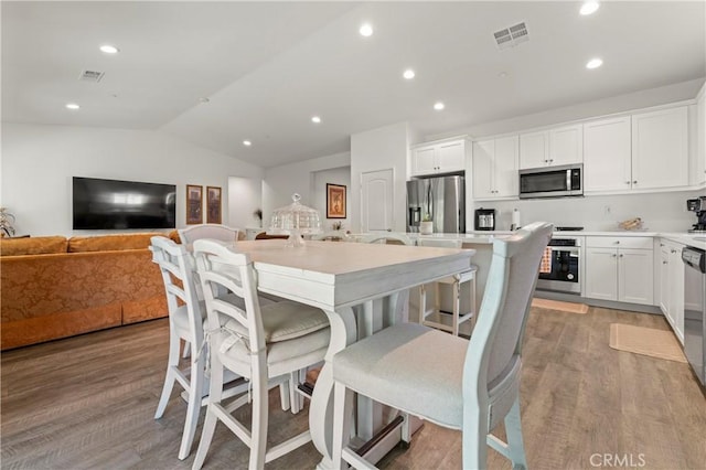 kitchen with light hardwood / wood-style flooring, appliances with stainless steel finishes, white cabinetry, a center island, and a kitchen bar