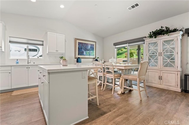 kitchen with a breakfast bar area, white cabinetry, a center island, vaulted ceiling, and light hardwood / wood-style flooring