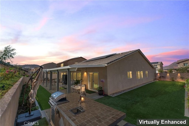 back house at dusk featuring an outdoor kitchen, sink, a patio, and a lawn