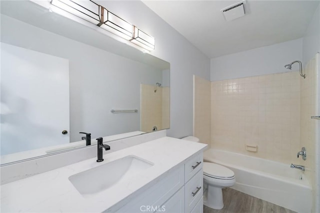 full bathroom with tiled shower / bath combo, vanity, hardwood / wood-style floors, and toilet