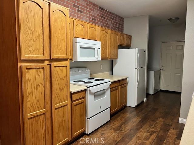 kitchen featuring white appliances, brick wall, and dark hardwood / wood-style flooring