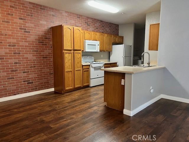 kitchen featuring brick wall, sink, kitchen peninsula, dark wood-type flooring, and white appliances