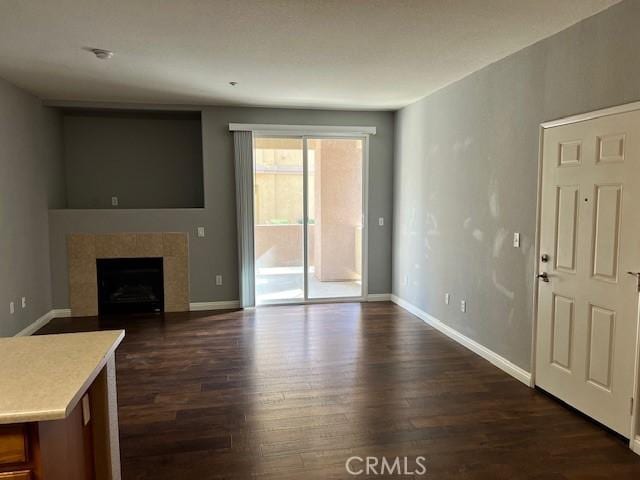 unfurnished living room featuring dark hardwood / wood-style flooring and a tiled fireplace