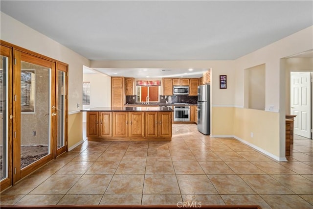 kitchen featuring light tile patterned flooring, appliances with stainless steel finishes, kitchen peninsula, and backsplash