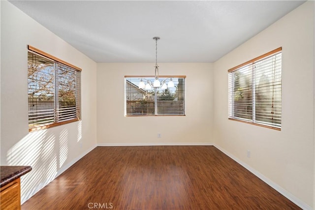 unfurnished dining area featuring a healthy amount of sunlight, dark hardwood / wood-style floors, and a chandelier