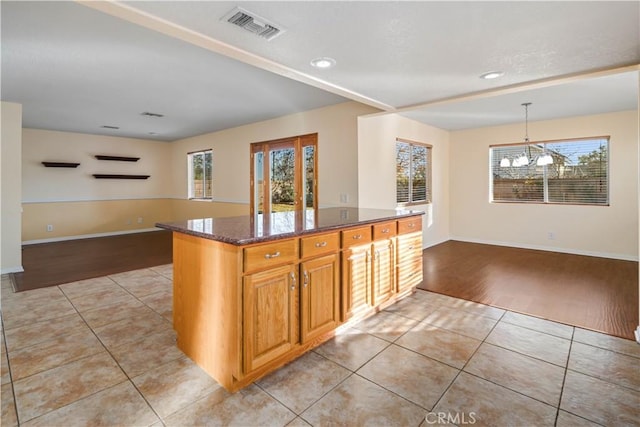 kitchen featuring light tile patterned flooring, a center island, a chandelier, pendant lighting, and dark stone counters