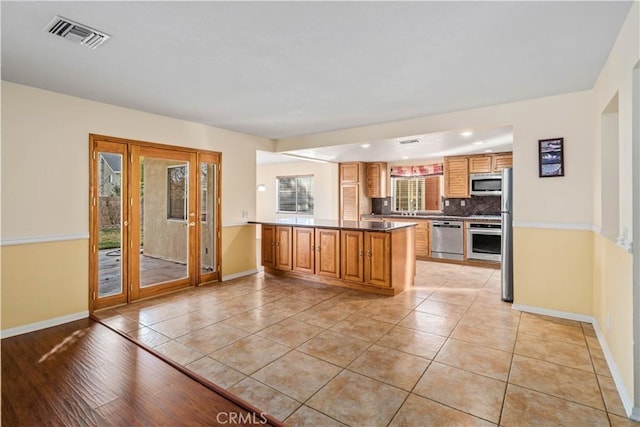 kitchen featuring light tile patterned flooring, stainless steel appliances, kitchen peninsula, and backsplash