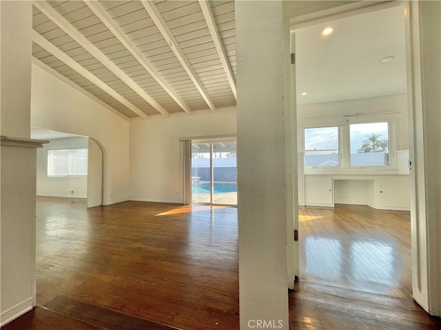 spare room featuring beam ceiling, dark wood-type flooring, and a wealth of natural light