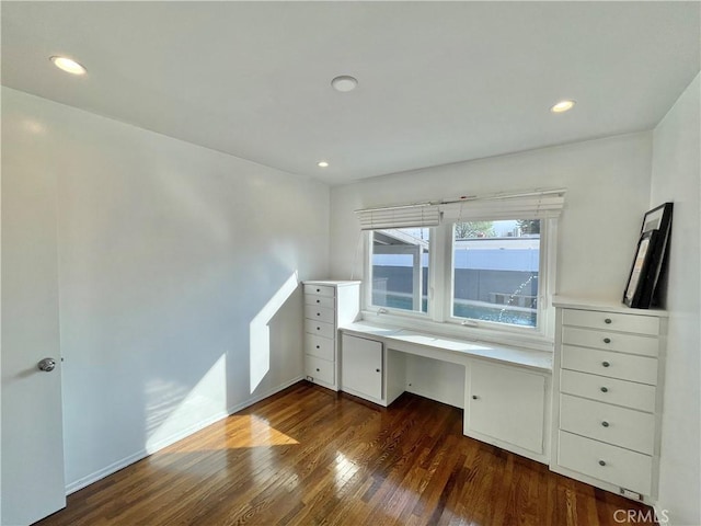 unfurnished office featuring built in desk and dark hardwood / wood-style flooring