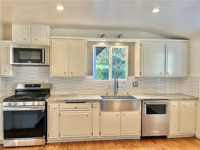 kitchen with sink, appliances with stainless steel finishes, white cabinetry, light stone countertops, and light wood-type flooring