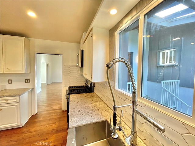 kitchen with white cabinetry, gas stove, light stone counters, and light hardwood / wood-style flooring