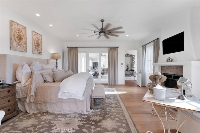 bedroom with access to exterior, light hardwood / wood-style flooring, a brick fireplace, and ceiling fan