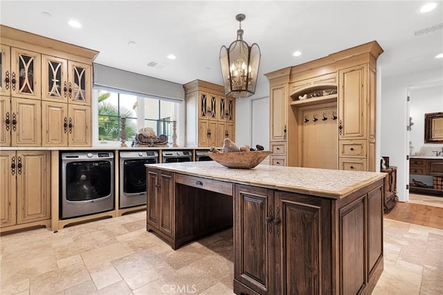 kitchen featuring a kitchen island, pendant lighting, washing machine and dryer, light stone countertops, and an inviting chandelier