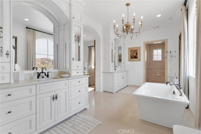 bathroom with an inviting chandelier, a healthy amount of sunlight, vanity, and a bathing tub