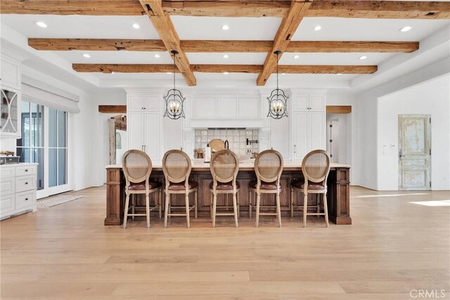 kitchen with light hardwood / wood-style flooring, a breakfast bar, white cabinetry, decorative light fixtures, and a large island with sink