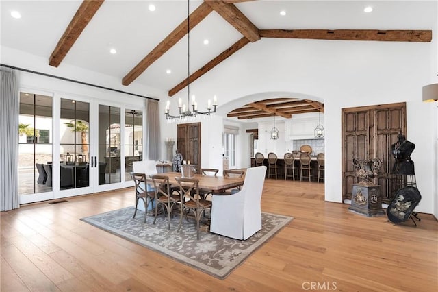 dining space with beam ceiling, high vaulted ceiling, a chandelier, and light hardwood / wood-style floors