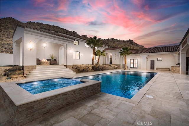 pool at dusk featuring an in ground hot tub and a patio area