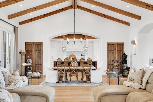 living room with beam ceiling, a notable chandelier, high vaulted ceiling, and light hardwood / wood-style flooring