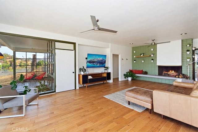 living room featuring a tiled fireplace, ceiling fan, and light wood-type flooring