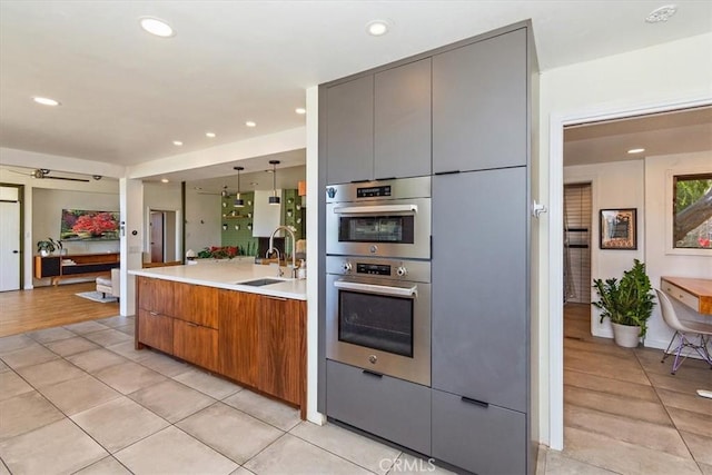 kitchen with light tile patterned flooring, gray cabinets, sink, and hanging light fixtures