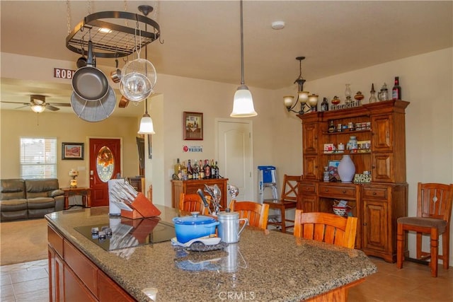 kitchen with light tile patterned flooring, a center island, pendant lighting, ceiling fan, and light stone countertops