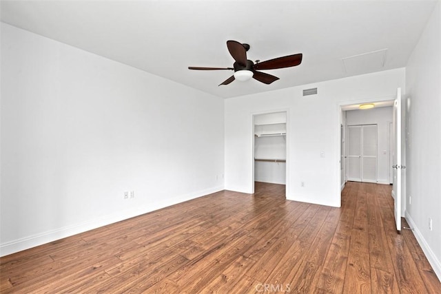 unfurnished bedroom featuring ceiling fan, a walk in closet, dark hardwood / wood-style flooring, and a closet