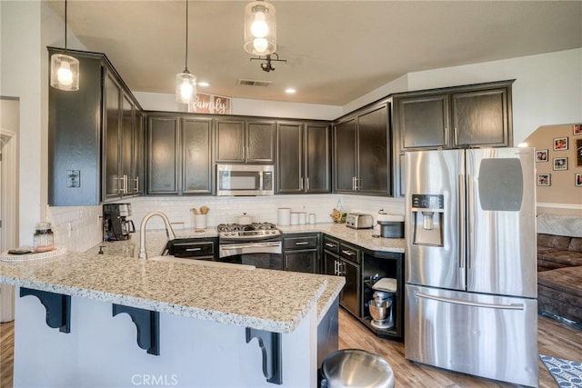 kitchen featuring pendant lighting, appliances with stainless steel finishes, light stone countertops, and tasteful backsplash