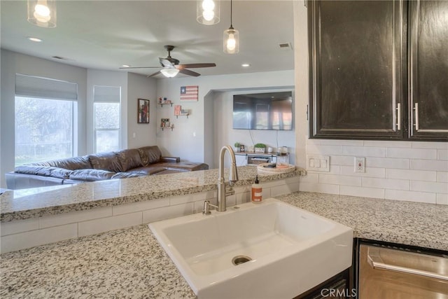 kitchen with pendant lighting, tasteful backsplash, sink, dark brown cabinetry, and light stone countertops