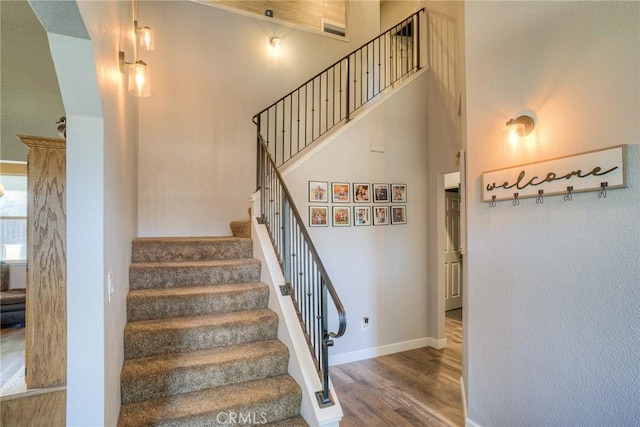 stairs featuring a towering ceiling and wood-type flooring