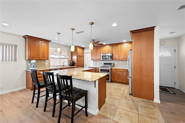 kitchen featuring decorative light fixtures, a center island, a kitchen breakfast bar, stainless steel appliances, and light stone countertops