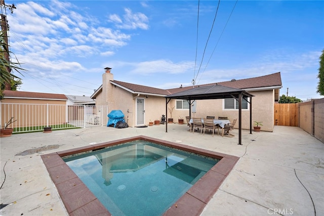 rear view of property featuring a gazebo, an in ground hot tub, and a patio