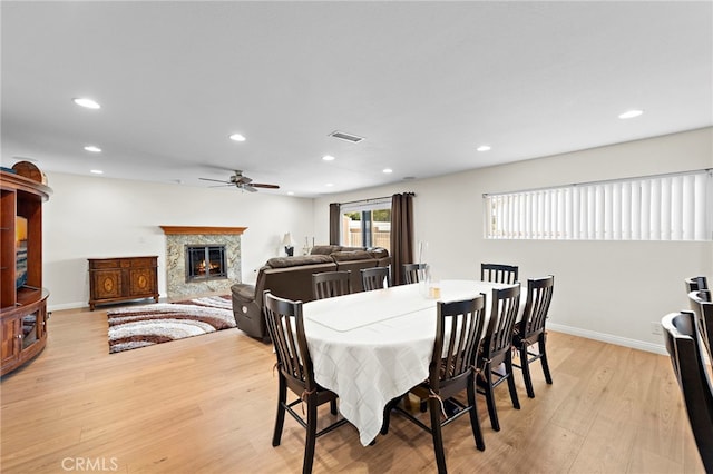 dining space with a high end fireplace, light hardwood / wood-style floors, and ceiling fan