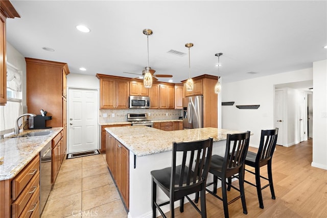 kitchen with sink, stainless steel appliances, a center island, light stone countertops, and decorative light fixtures