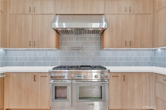 kitchen with tasteful backsplash, wall chimney exhaust hood, double oven range, and light brown cabinets