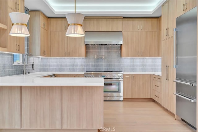 kitchen featuring wall chimney exhaust hood, high quality appliances, hanging light fixtures, and light brown cabinets