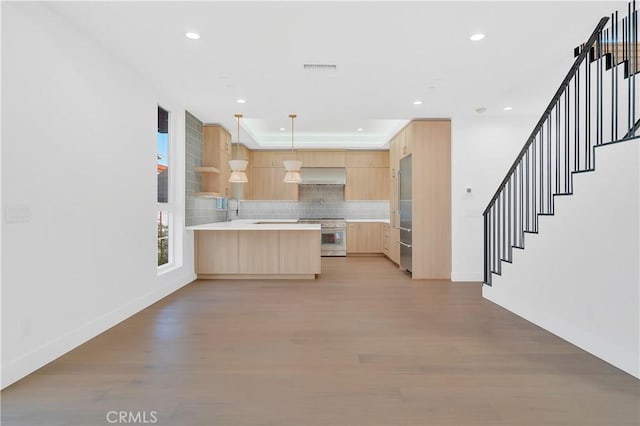 kitchen featuring wall chimney exhaust hood, light brown cabinetry, high quality appliances, kitchen peninsula, and pendant lighting