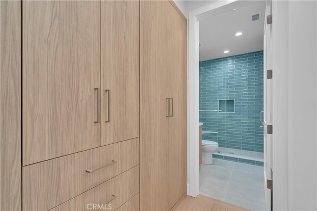 bathroom featuring tiled shower, tile patterned floors, and toilet