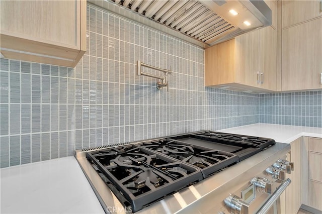 kitchen featuring backsplash, wall chimney exhaust hood, stovetop, and light brown cabinets