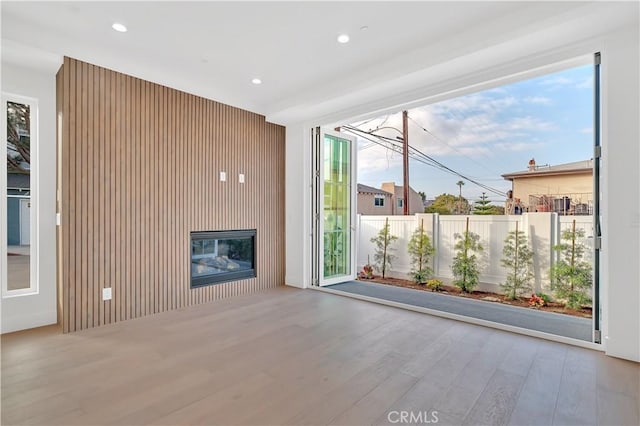 unfurnished living room with a healthy amount of sunlight, light hardwood / wood-style floors, and wood walls