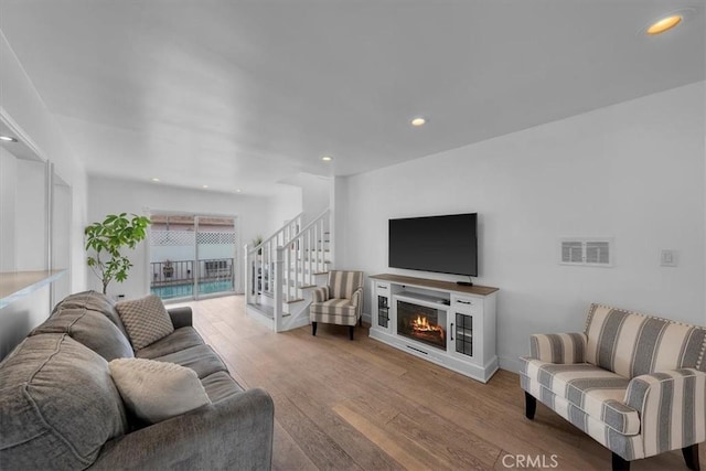 living area with hardwood / wood-style flooring, recessed lighting, visible vents, a lit fireplace, and stairway