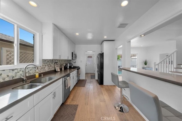 kitchen with stainless steel appliances, white cabinetry, sink, and backsplash