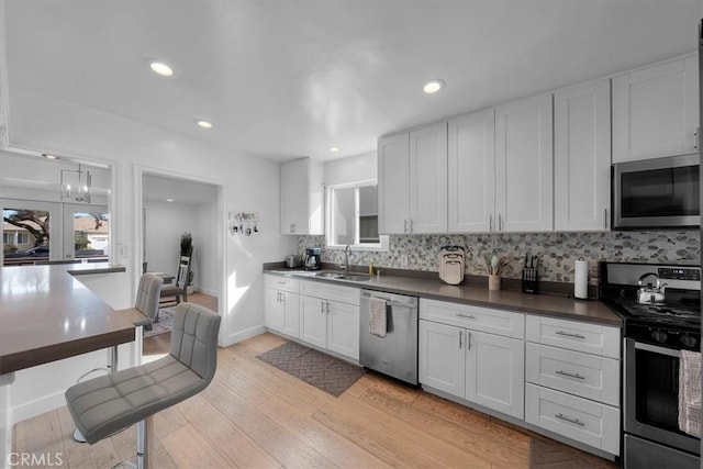 kitchen with sink, light wood-type flooring, white cabinets, and appliances with stainless steel finishes