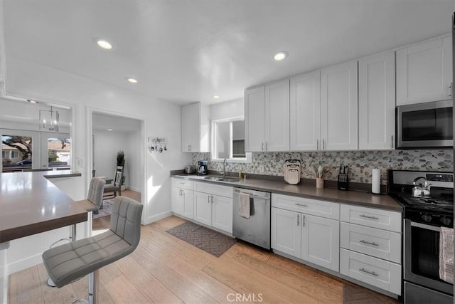 kitchen with dark countertops, light wood-style flooring, appliances with stainless steel finishes, white cabinetry, and a sink