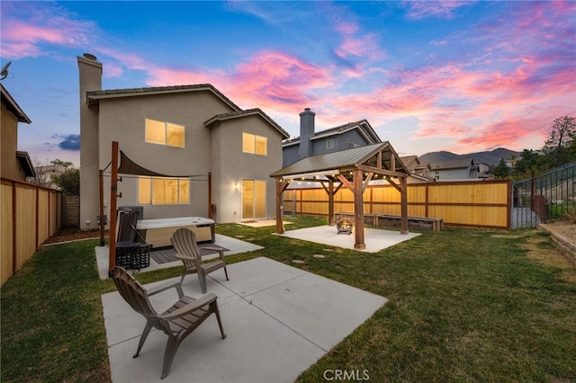 back house at dusk featuring a hot tub, a gazebo, a yard, and a patio area