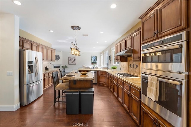 kitchen featuring appliances with stainless steel finishes, pendant lighting, a kitchen breakfast bar, a center island, and light stone countertops