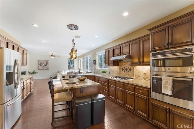 kitchen featuring a breakfast bar area, decorative light fixtures, appliances with stainless steel finishes, a kitchen island, and backsplash