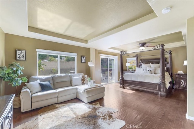 bedroom featuring hardwood / wood-style flooring, access to exterior, and a tray ceiling